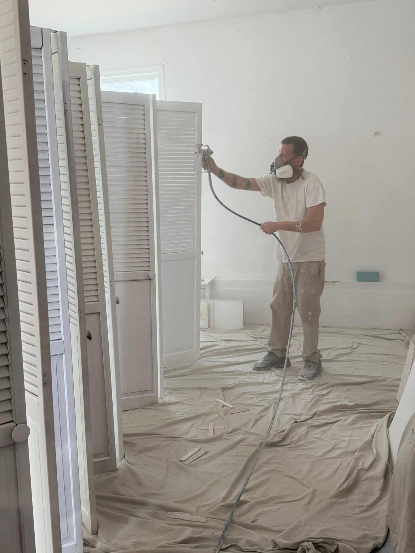 Jon Hammond spray-finishing louvered doors on a fully masked job site